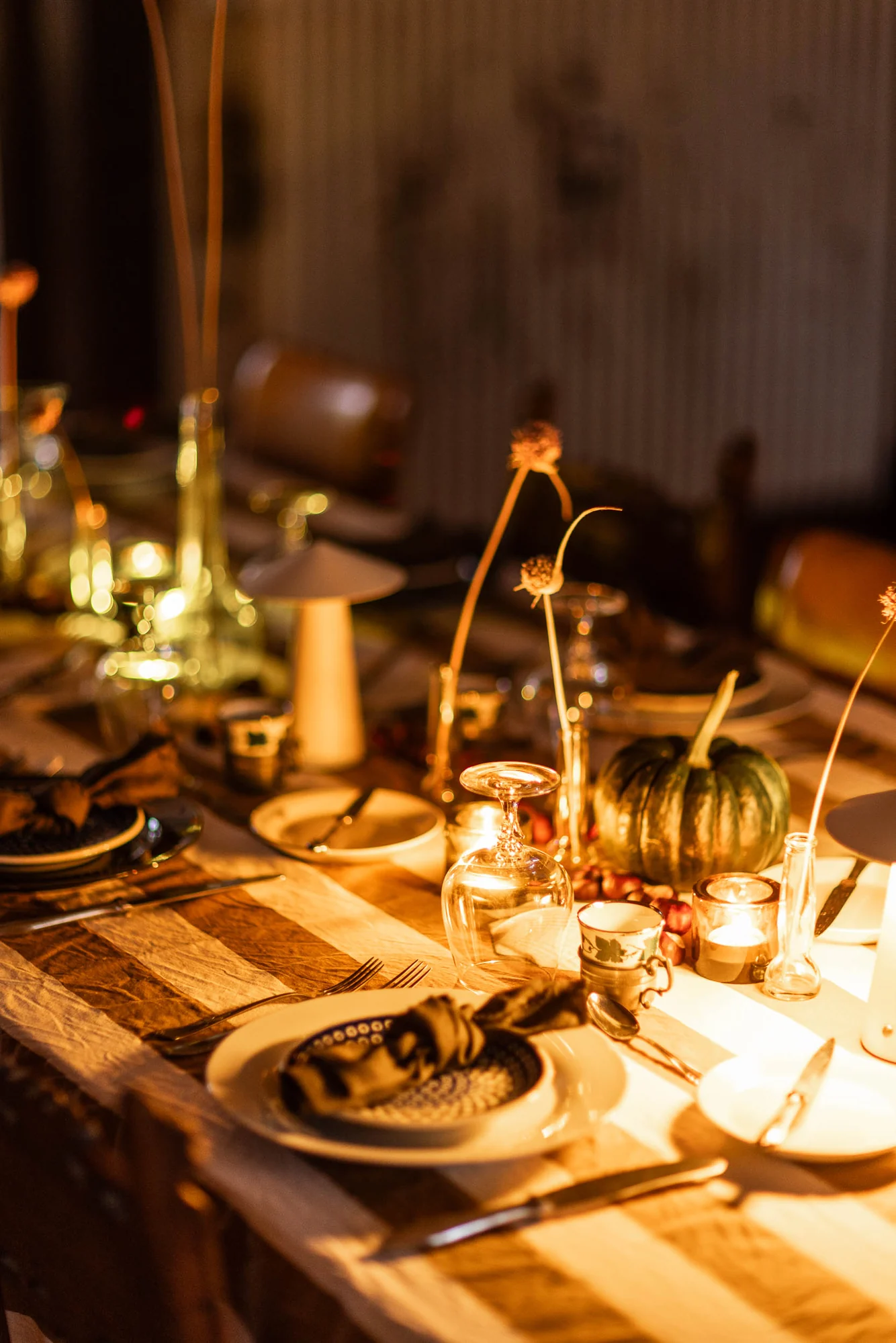 Table detail at dusk with a small green squash, rosehips, a tealight, dried allium stems and a knotted napkin on the plate