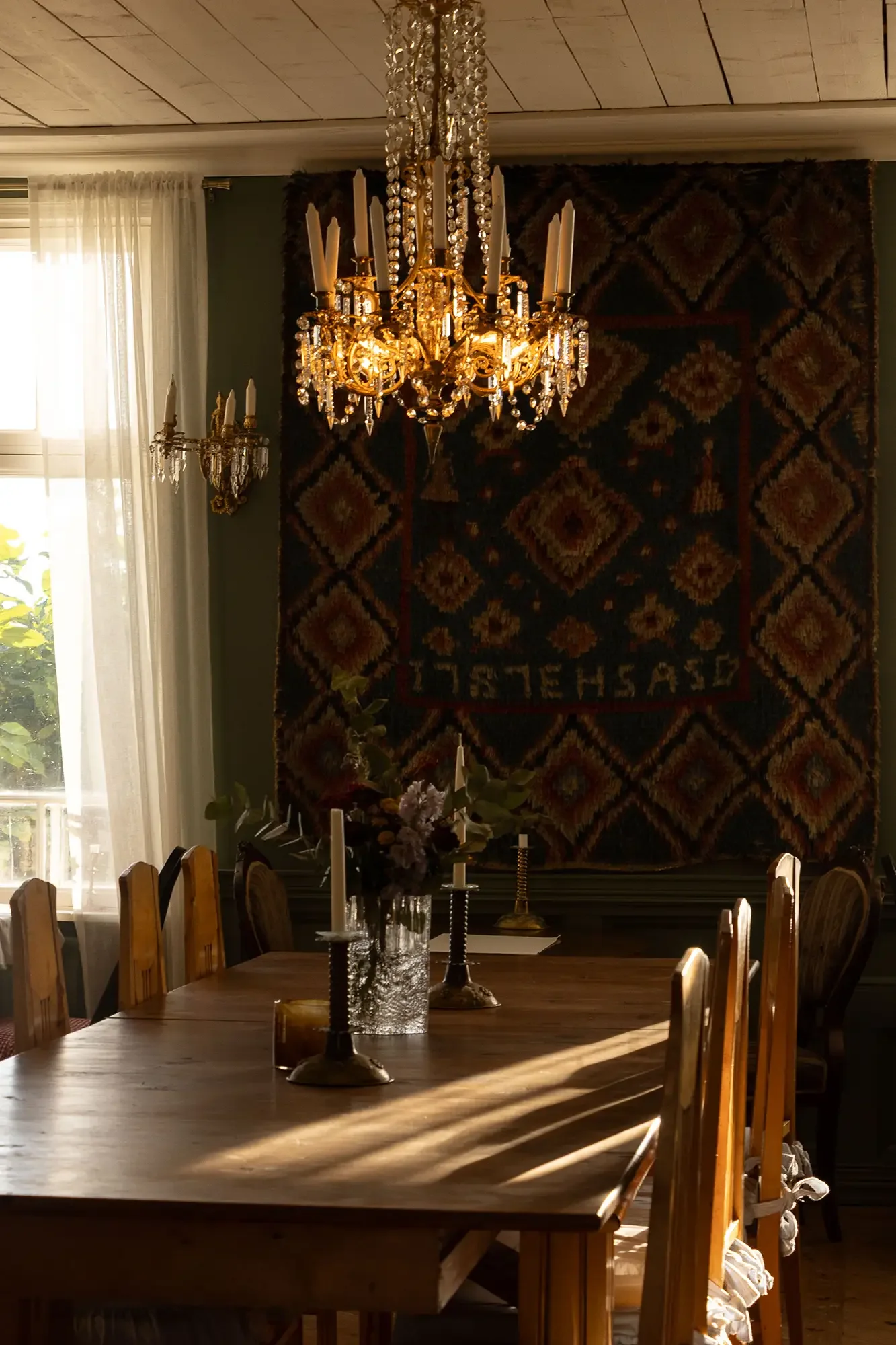 Speisesaal mit Kristallleuchter, langem Holztisch und großem gemustertem Wandteppich
