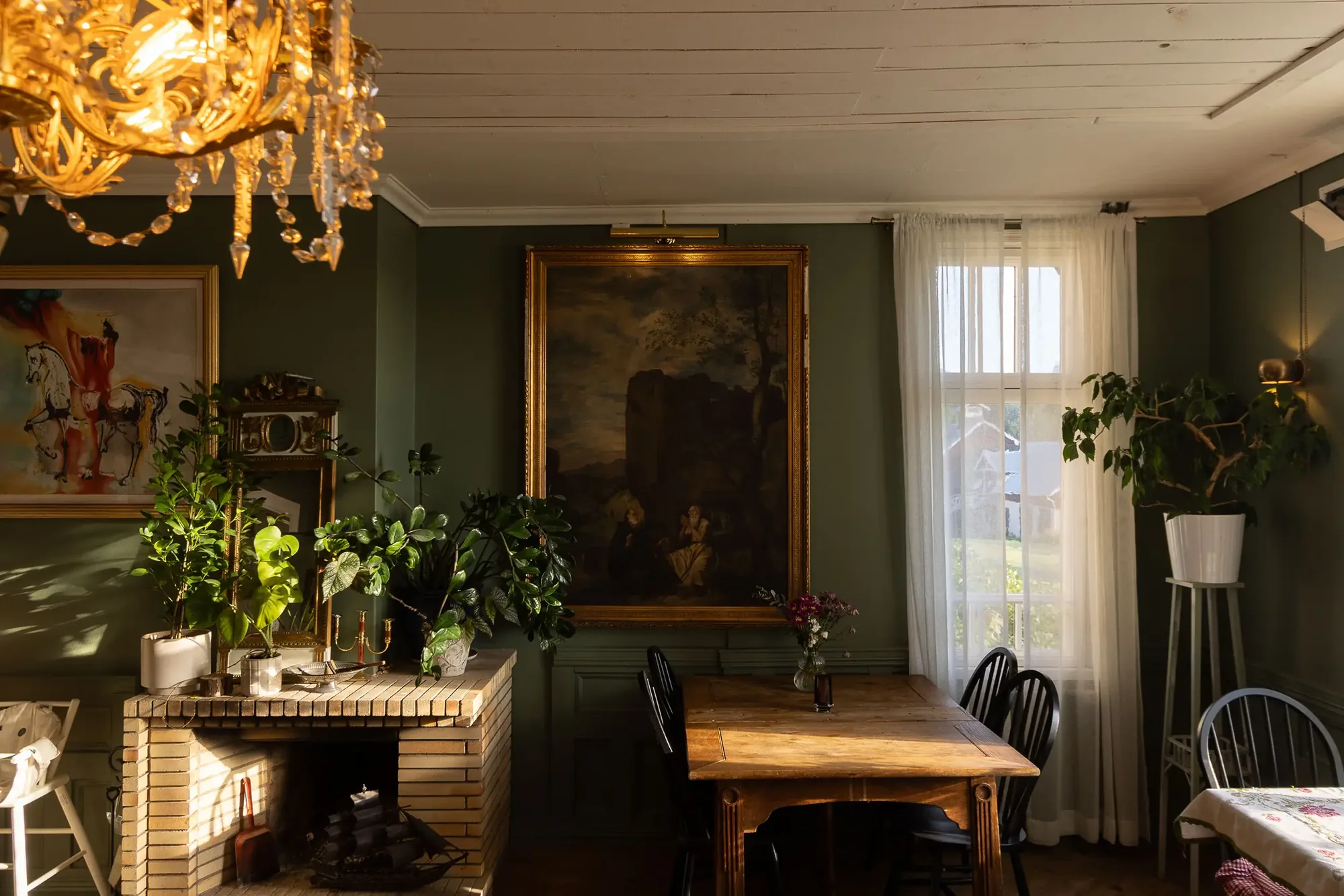 Grün gestrichener Raum mit großem dunklem Gemälde, Pflanzen, Holztisch und schwarzen Stühlen