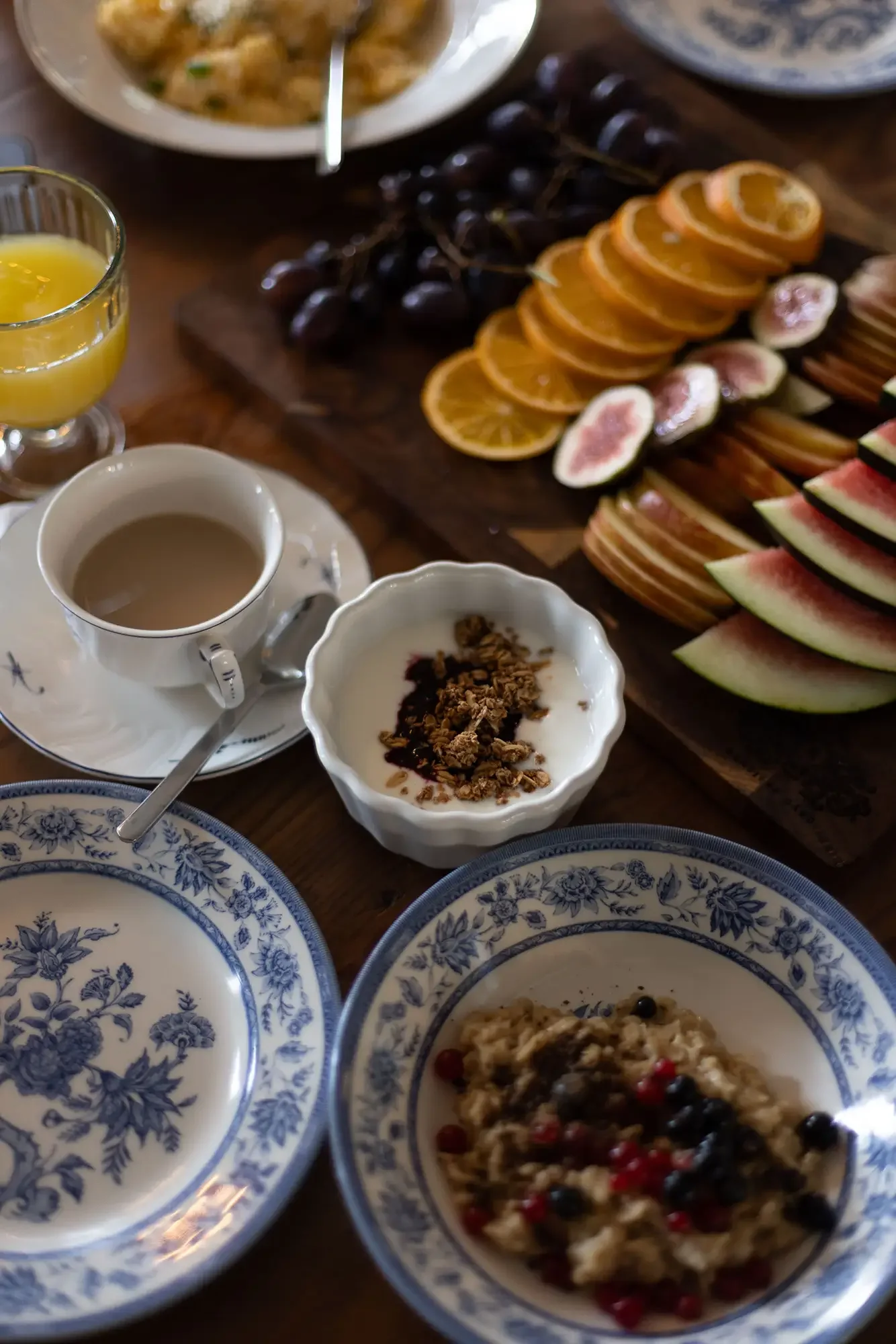 Frühstückstafel mit Obstbrett, Feigen, Melone, Porridge und Kaffee auf blau-weißem Porzellan