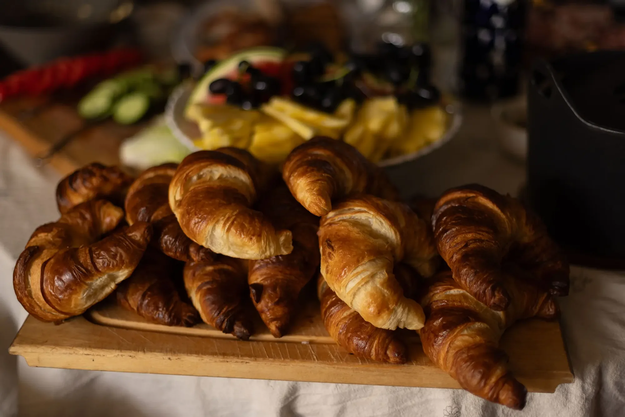 Frisch gebackene Croissants auf einem Holzbrett neben Obstplatten