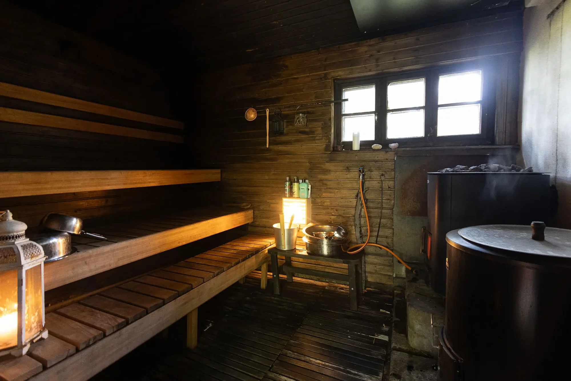 Innenraum der holzbefeuerten Sauna aus dem 19. Jahrhundert mit Kerzenlaterne, Holzbänken und Wasserkessel